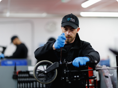 A photograph of a warehouse technician making adjustments to the wheels on a manual wheelchair.