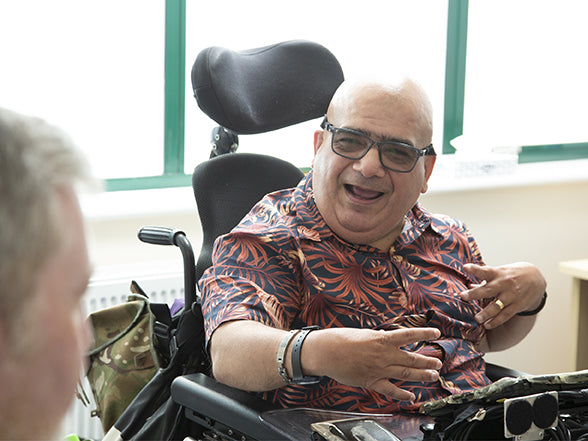 Man in a powered wheelchair smiling at another person, just out of shot