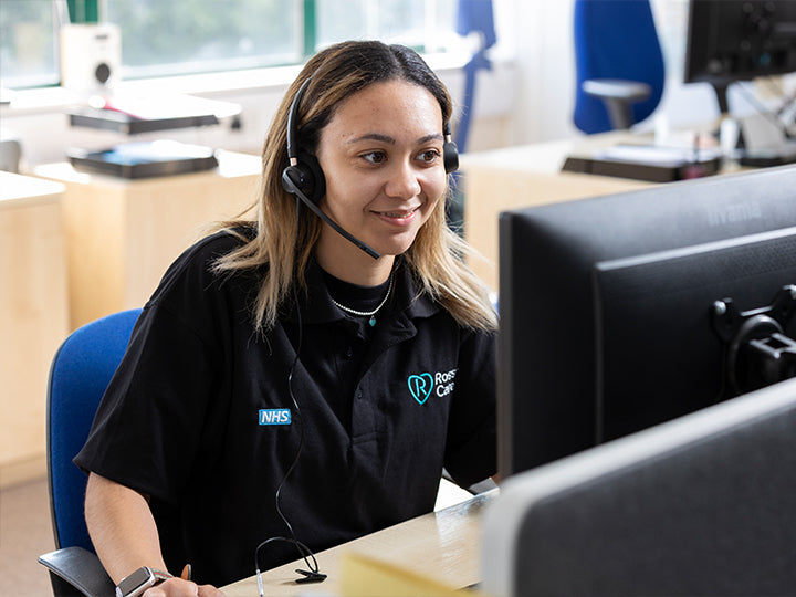 Smiling Customer Services colleague working at a computer wearing a call headset