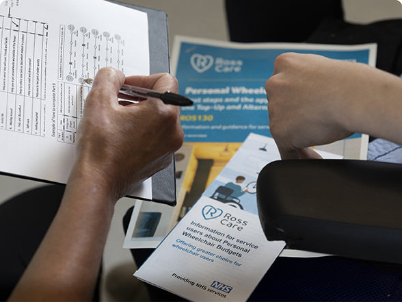 Ross Care clinician showing a service user the WATCh form and Personal Wheelchair Budget information leaflets